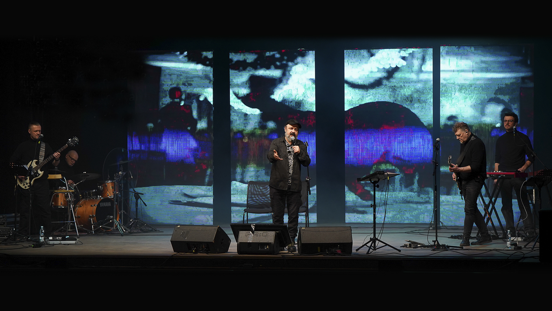 Romeo i Julia żyją. Na zdjęciu po środku Arkadiusz Jakubik z mikrofonem w ręku. Po lewej stronie stoi gitarzysta i perkusista po prawej gitarzysta i klawiszowiec. Z tyłu za aktorem są wyświetlane projekcje