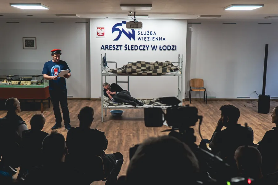W sali konferencyjnej z napisem „Służba Więzienna Areszt Śledczy w Łodzi” odbywa się prezentacja przed publicznością siedzącą tyłem. Na środku stoi mężczyzna czytający scenariusz, a obok niego na łóżku piętrowym leży druga osoba.