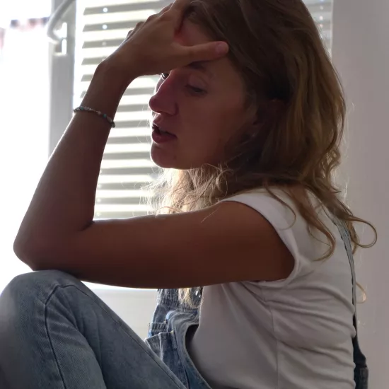 Zdjęcie przedstawia próbę stolikową do spektaklu „Ifigenia ze Splott”. Na krześle z jedną zgiętą nogą pod sobą siedzi bokiem Agnieszka Skrzypczak. Druga noga, również jest zgięta i spoczywa na niej łokieć. Dłoń aktorki ze zgiętego łokcia podpiera jej czoło. Usta Agnieszki Skrzypczak są lekko otwarte a wzrok spuszczony na dół. 