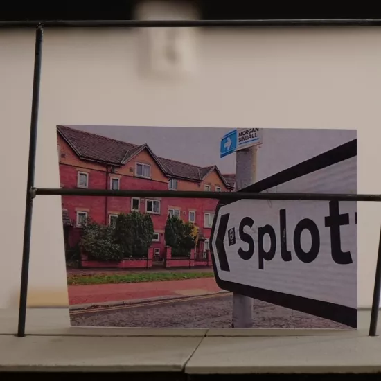 Zdjęcie przedstawia próbę stolikową do spektaklu „Ifigenia ze Splott”. Zdjęcie skoncentrowane na makiecie osiedlowego trzepaka, na którym opiera się fotografia brytyjskiej kamienicy, którą poprzedza znak z nazwą dzielnicy Splott.