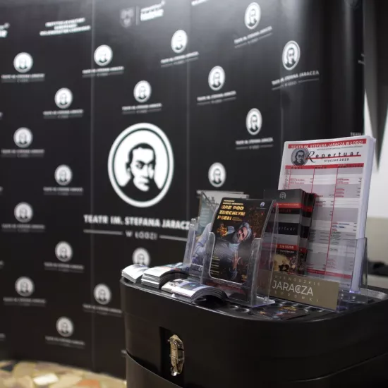 Zdjęcie przedstawia ściankę reklamową Teatru Jaracza w Łodzi i materiały promocyjne 