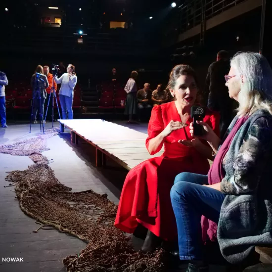 Zdjęcie z próby medialnej spektaklu „Zamiana" wykonane na Scenie Kameralnej, w scenografii spektaklu. Na drewnianym pomoście siedzi aktorka Ewa Audykowska-Wiśniewska wraz z dziennikarką Małgorzata Warzecha. W tle widać innych dziennikarzy przeprowadzających wywiady z innymi aktorami. 