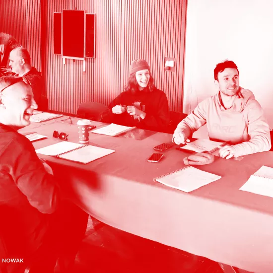 zdjęcie przedstawia pierwszą próbę spektaklu "Morderstwo w hotelu". Przy stole siedzą aktorzy. Tyłem do obiektywu siedzi śmiejący się aktor Mariusz Witkowski. Po prawej stronie stołu, przy stole stoi pracownik teatru Marcin Majczak, obok siedzi scenograf Grzegorz Policiński. Na krzesłach obok siedzą aktorzy Natalia Klepacka i Krzysztof Wach. Na stole znajdują się egzeplarze tekstu. Na zdjęcie nałożony został czerwony filtr. 