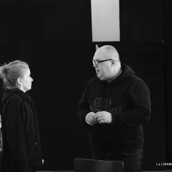 zdjęcie przedstawia próbę spektaklu „Świętoszek". Zostało zrobione na dużej sali prób w Teatrze Jaracza w Łodzi. Na zdjęciu stoją aktorzy Sara Lityńska, z wystraszoną miną oraz Paweł Tucholski. Na zdjęciu widać także Katrzynę Brudek i Marka Nędzę. 