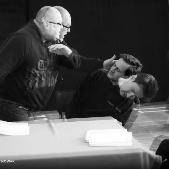 zdjęcie przedstawia próbę spektaklu „Świętoszek" w reżyserii Magdaleny Piekorz. Jest delikatnie rozmyte, ponieważ zostało zrobione w ruchu. Na zdjęciu Paweł Tucholski stoi nad aktorem Markiem Nędzą w geście jakby chciał go uderzyć, Marek Nędza uchyla się.  Autorem zdjęcia jest Marcin Nowak