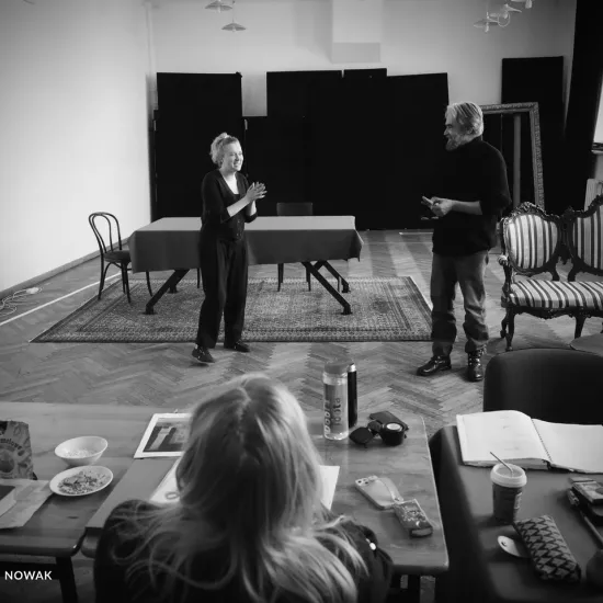 zdjęcie przedstawia próbę spektaklu „Świętoszek" w reżyserii Magdaleny Piekorz. Na zdjęciu tyłem do aparatu widać inspicjentkę Katarzynę Brudek, która siedzi za stołem, na którym widać egzemplarz sztuki. Przed stołem, w niedalekiej odległości stoją aktorzy Iwona Karlicka i Dariusz Bereski