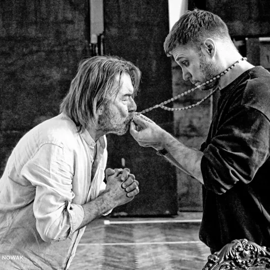 próba do spektaklu „Świętoszek", na zdjęciu: Bogusław Suszka całujący krzyż od różańca, który mu podaje Łukasz Stawowczyk, fot. Marcin Nowak. Zdjęcie jest czarno-białe