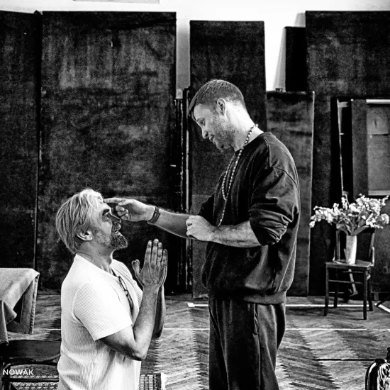 próba do spektaklu „Świętoszek", na zdjęciu: Dariusz Bereski, który klęczy i Łukasz Stawowczyk wykonujący gest błogosławieństwa na jego czole, fot. Marcin Nowak. Zdjęcie jest czarno-białe