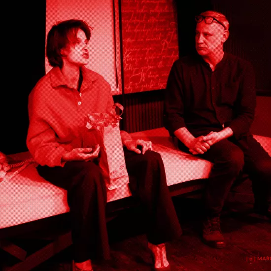 próba do spektaklu „Morderstwo w hotelu", zdjęcie zostało wykonane w sali prób, na zdjęciu: Natalia Klepacka, Mariusz Witkowski. Aktorzy siedzą obok siebie na łóżku. Aktorka ma między nogami papierową torbę z jedzeniem. Twarz ma zwróconą w przód. Aktor patrzy na nią, fot. Marcin Nowak. Na zdjęcie nałożony jest czerwony filtr. 