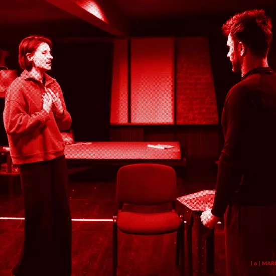 próba do spektaklu „Morderstwo w hotelu", zdjęcie zostało zrobione w sali prób,na zdjęciu: Natalia Klepacka, Krzysztof Wach. Aktorzy stoją od siebie w odległości, twarzami zwróconymi do siebie. Natalia Klepacka ma przyciągnięte do klatki piersiowej ręce, fot. Marcin Nowak. Na zdjęcie nałożony jest czerowny filtr. 