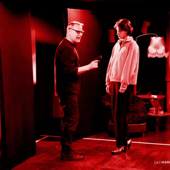 próba do spektaklu „Morderstwo w hotelu", zdjęcie zostało zrobione w sali prób, na zdjęciu: Mariusz Witkowski trzymający w ręku pistolet i Natalia Klepacka, fot. Marcin Nowak. Na zdjęcie nałożony jest czerwony filtr.