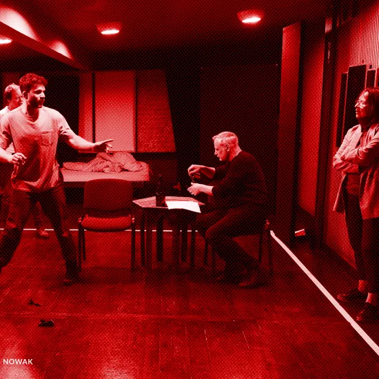 próba spektaklu „Morderstwo w hotelu", zdjęcie zostało wykonane w sali prób, na zdjęciu Krzysztof Wach, z tyłu reżyser Jacek Bończyk, siedzący na krześle przy niskim stole Mariusz Witkowski oraz stojąca przy ścianie Bogusława Pawelec, fot. Macin Nowak. Na zdjęcie nałożony jest czerwony filtr.