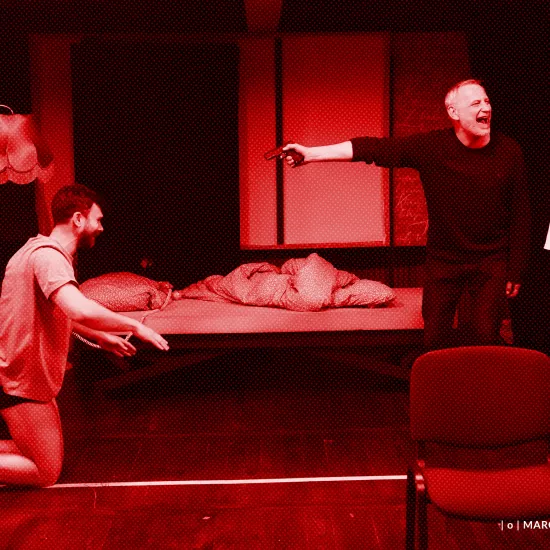 próba spektaklu „Morderstwo w hotelu", zdjęcie zostało wykonane w sali prób, na zdjęciu Krzysztof Wach, który ma na sobie koszulkę i bokserki, klęczy. Mariusz Witkowski celuje pistoletem do Krzysztofa Wacha, przy nim stoi Natalia Klepacka. fot. Macin Nowak. Na zdjęcie został nałożony czerwony filtr.