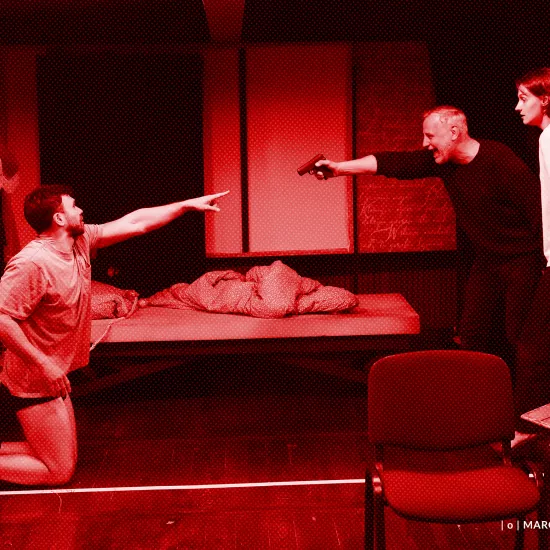 próba spektaklu „Morderstwo w hotelu", zdjęcie zostało wykonane w sali prób, na zdjęciu Krzysztof Wach, który ma na sobie koszulkę i bokserki, klęczy i wskazuje palcem na Mariusza Witkowskiego, Mariusz Witkowski celuje pistoletem do Krzysztofa Wacha, przy nim stoi Natalia Klepacka. fot. Macin Nowak. Na zdjęcie został nałożony czerwony filtr.