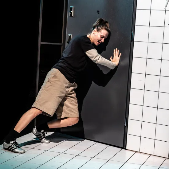 Zdjęcie ze spektaklu „Czas na wielki numer". Na fotografii widać aktorkę Natalię Klepacką, która blokuje ciałem drzwi wejściowe uniemożliwiając wejście osoby z zewnątrz. Jest o nie oparta lewym barkiem i przytrzymuje drzwi prawą ręką. Autorką fotografii jest Natalia Kabanow.