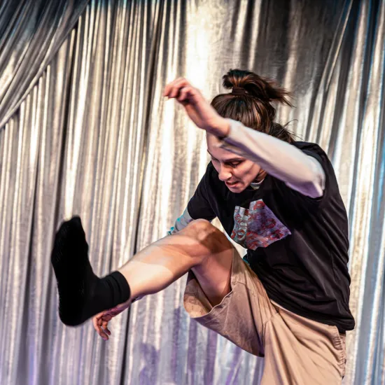 Zdjęcie ze spektaklu „Czas na wielki numer". Na fotografii sktorka Natalia Klepacka jest uchwycona w pozie jakby walczyła. Prawą nogę ma wysuniętą do przodu jakby zadawała nią cios. Lewą rękę ma uniesioną do góry. Jej sylwetka jest pochwylona do przodu. Autorką zdjęcia jest Natalia Kabanow