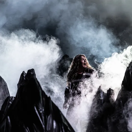 Zdjęcie przedstawia góry, wokół nich jest dużo dymu imitującego mgły. Pośród gór widać niewyraźnie aktorkę Milenę Lisiecką. Autorką zdjęcia jest Natalia Kabanow